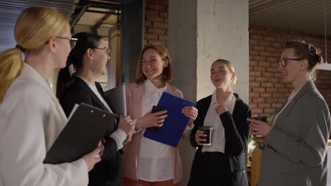 A-group-of-confident-business-girls-in-glasses-and-business-suits-stand-in-a-semicircle-and-chat-during-a-break-from-work-in-a-modern-office