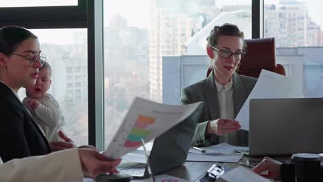 Active-meeting-of-businesswomen-at-a-table-in-the-office-to-solve-case-and-task.-A-confident-middle-aged-girl-in-glasses-and-a-business-suit,-the-leader-of-a-businesswoman-group-sits-at-the-table-and-takes-work-and-plans-schedules