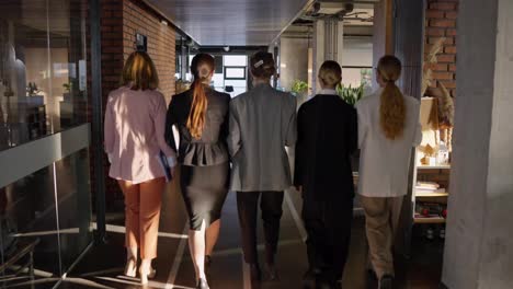 Rear-view-of-five-confident-businesswomen-walking-on-gray-floor-in-modern-office-confident.-Five-confident-girls-in-business-suits-walk-through-the-office