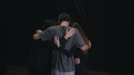 A-group-of-confident-young-actors-in-black-clothes-together-with-their-stage-director,-hug-and-collect-their-thoughts-before-performing-in-a-play-and-theater