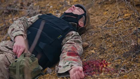 A-soldier-in-camouflage-uniform-and-black-body-armor-seriously-wounded-in-the-arm-is-rendered-unconscious-in-the-steppe-during-military-operations.-A-wounded-soldier-lies-and-waits-for-help-to-provide-first-aid-and-stop-blood-loss