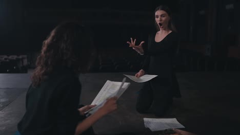 A-brunette-girl-communicates-with-her-colleague-while-acting-out-her-role-in-the-theater-and-preparing-the-text-and-script-for-a-performance-on-stage-in-an-empty-theater