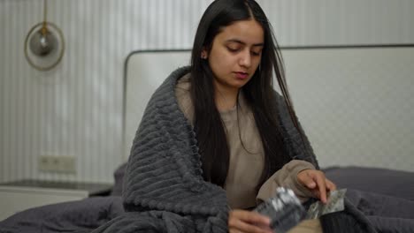 A-brunette-girl-with-a-sick-look-chooses-which-pills-she-should-take-takes-one-out-and-washes-it-down-with-water-in-a-modern-apartment-during-an-illness-in-the-bedroom