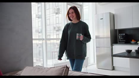 A-happy-brunette-girl-in-a-dark-green-jacket-brings-a-transparent-glass-of-water-for-her-elderly-father-in-gray-hair-and-a-pink-shirt-in-a-modern-apartment