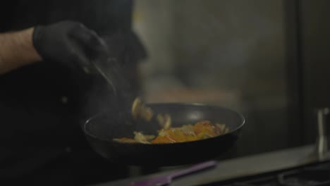 Close-up-of-a-professional-male-chef-stirs-vegetables-that-he-fries-with-a-lot-of-controlled-heat-after-adding-alcohol-to-a-dish-in-a-restaurant-kitchen.-A-large-flame-comes-from-a-hot-frying-pan-during-a-flambéed-dish