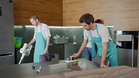 A-confident-company-of-three-cleaners-in-a-black-apron-two-guys-and-a-brunette-girl-cleaning-a-modern-kitchen-and-putting-things-in-order-in-a-modern-apartment-on-call