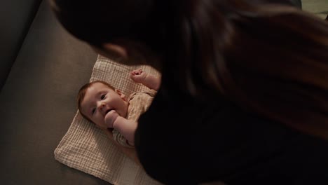 Top-view-mom-puts-her-little-baby-daughter-on-a-special-mat-in-a-brown-overalls-and-prepares-clothes-to-change-clothes-on-her-little-baby-daughter