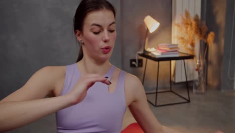 Close-up-a-confident-brunette-girl-with-an-athletic-build-in-a-purple-sports-top-uses-a-red-mat-and-does-sports-and-pumps-up-her-abs-in-a-modern-apartment-at-home