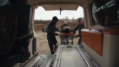 View-from-the-side-of-the-ambulance-cabin-three-military-men-put-a-wounded-man-in-camouflage-uniform-on-a-snare-in-an-ambulance-while-providing-medical-care-on-the-battlefields