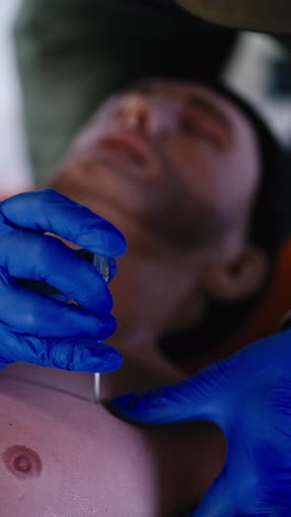 Vertical-video-Close-up-shot-of-a-male-medic-in-blue-elastic-gloves-on-a-male-doll-practicing-inserting-a-medical-needle-into-a-mans-chest-during-a-medical-military-course