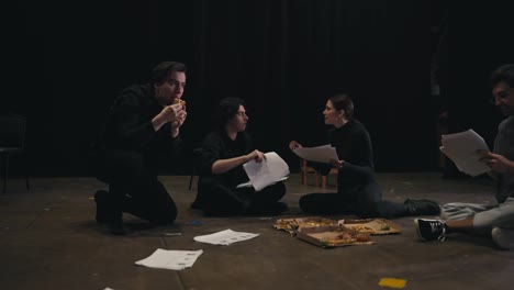 Confident-actor-brunette-girl-in-a-black-suit-communicates-with-her-colleague-about-the-script-holding-sheets-of-papers-in-her-hands-along-with-her-director-on-stage-at-a-rehearsal-in-the-theater