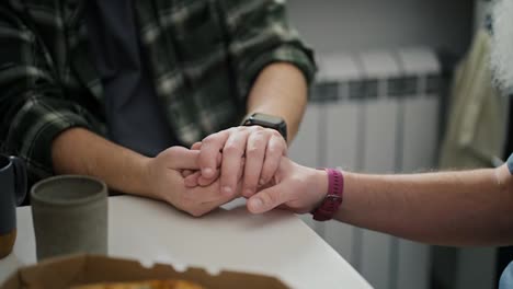 And-two-middle-aged-men-hold-hands-during-their-difficult-communication-And-their-relationship-in-the-kitchen-in-a-modern-apartment.-Relationships-and-mutual-understanding-during-a-difficult-conversation-about-relationships-in-an-LGBT-couple-of-two-men