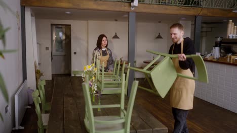 Un-Chico-Rubio-Y-Una-Chica-Morena-De-Color-Castaño-Claro-Están-Limpiando-Y-Arreglando-Sillas-En-El-Salón-De-La-Cafetería.