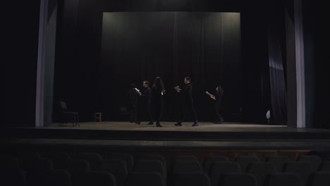 Confident-group-of-young-actors-in-black-suits-walk-in-a-circle-on-stage-in-the-theater-and-read-out-their-words-during-preparation-and-rehearsal-for-a-performance-in-the-theater