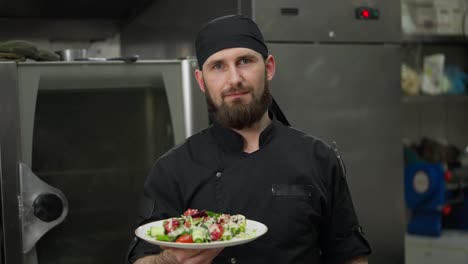 Retrato-De-Un-Chef-Profesional-Feliz-Con-Un-Uniforme-Negro-Con-Un-Plato-De-Ensalada-Preparado-En-Sus-Manos-Antes-De-Una-Presentación-En-La-Cocina-De-Un-Restaurante.