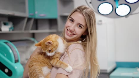 Portrait-of-a-happy-blonde-girl-holding-an-orange-white-cat-in-her-arms-during-an-appointment-at-a-veterinary-clinic-examining-pets