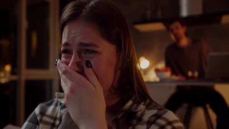 A-brunette-girl-in-a-plaid-shirt-cries-while-watching-a-sad-drama-on-TV-and-her-brunette-boyfriend-in-a-gray-T-shirt-consoles-the-girl-and-hugs-her-in-a-modern-studio-apartment-in-the-evening