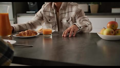 Close-up-of-a-young-man-with-Black-skin-color-in-a-beige-plaid-shirt-and-a-young-adult-girl-holding-hands-during-their-breakfast-together-at-a-black-kitchen-table-in-a-modern-apartment