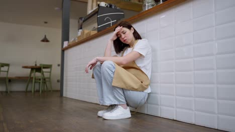 Tired-girl-brunette-waitress-sits-near-the-cash-register-and-rubs-her-forehead-with-her-hands-during-a-hard-day-at-work-in-a-cafe