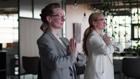 Side-view-of-a-confident-group-of-businesswomen-in-business-clothes-doing-yoga-during-a-short-break-between-work-in-a-modern-office