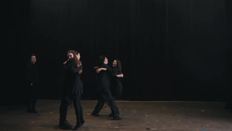 Jóvenes-Estudiantes-Y-Actores-De-La-Universidad-De-Teatro-Suben-Al-Escenario-Con-Trajes-Negros-Y-Se-Saludan-Y-Abrazan.-Un-Grupo-De-Actores-Sube-Al-Escenario-Y-Se-Saludan-Antes-Del-Comienzo-De-Un-Ensayo-Y-Una-Clase-En-La-Universidad-De-Teatro.