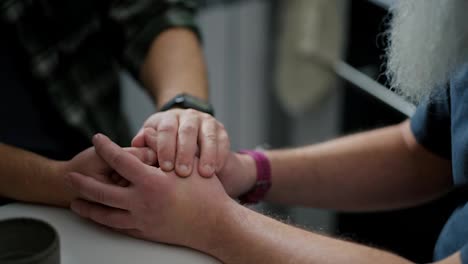 Close-up-elderly-and-middle-aged-men-hold-hands-during-their-difficult-conversation-about-relationships-and-relationships-in-LGBT-couples-of-two-men-in-the-kitchen-at-the-table-during-the-day