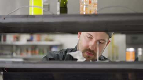 A-cook-in-a-black-uniform-with-a-beard-puts-all-checked-and-issued-orders-on-a-needle-in-the-kitchen-in-a-restaurant.-A-professional-chef-reviews-orders-and-removes-completed-orders