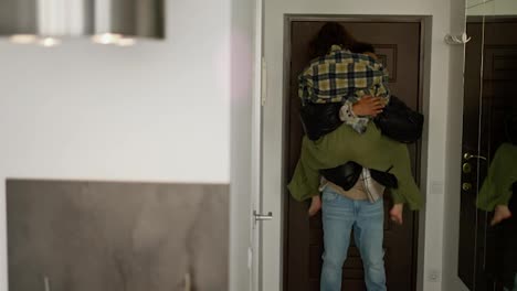 A-happy-young-brunette-girl-with-a-bob-hairstyle-in-a-plaid-shirt-runs-and-hugs-her-young-boyfriend-with-Black-skin-a-brunette-in-a-black-jacket-who-came-home-and-after-work-in-the-evening