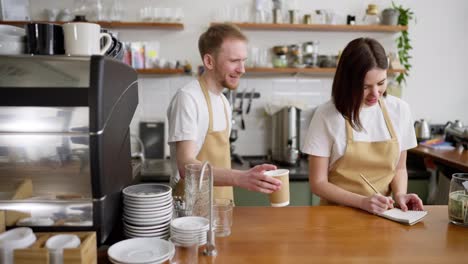 Un-Hombre-Rubio-Con-Un-Delantal-De-Barista-Amarillo-Le-Da-Un-Pedido-A-Una-Camarera-Y-Comienzan-A-Bailar-Juntos-En-El-Mostrador-De-Un-Café.