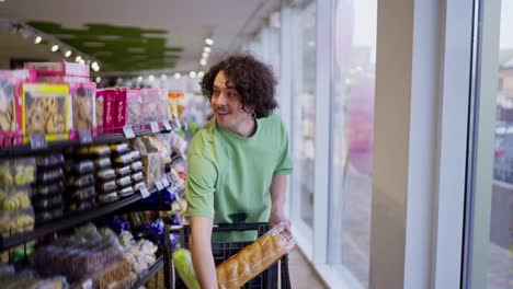 A-brunette-guy-with-curly-hair-walks-with-a-filled-cart-and-chooses-goods-while-shopping-in-a-grocery-supermarket