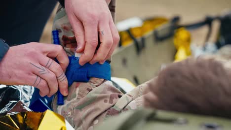 Nahaufnahme-Eines-Selbstbewussten-Männlichen-Sanitäters-In-Dunkelblauer-Uniform,-Der-Einen-Verband-Auf-Die-Verletzte-Hand-Eines-Soldaten-Legt,-Um-Blutverlust-Bei-Kampfhandlungen-Außerhalb-Der-Stadt-Zu-Vermeiden