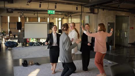 A-group-of-confident-girls-in-business-suits-dance-during-a-break-at-work-on-a-gray-carpet-during-a-happy-time-at-work-in-a-modern-office