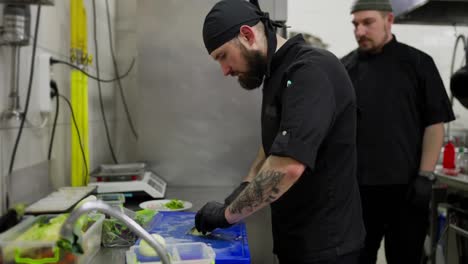 A-professional-male-chef-in-a-black-uniform-chops-onions-and-other-vegetables-while-starting-to-prepare-a-restaurant-for-work.-Chefs-work-in-the-kitchen-cutting-vegetables-and-preparing-dishes