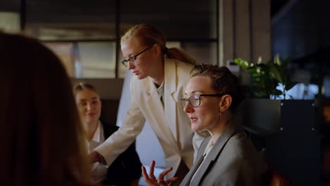 Side-view-of-a-confident-middle-aged-blonde-girl-in-glasses-and-a-business-uniform-talking-with-her-colleagues-during-a-meeting-about-work-and-a-meeting-in-a-modern-office