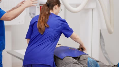 A-confident-brunette-girl-with-round-glasses-and-in-a-blue-uniform-performs-fluorography-together-with-her-colleague-doctor-of-a-young-brunette-girl-in-a-modern-clinic