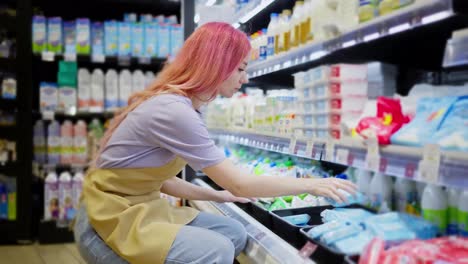 Confident-girl-supermarket-worker-distributes-dairy-products-on-the-store-counter.-A-bright-girl-with-red-hair-works-in-a-supermarket