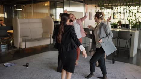 A-group-of-confident-businesswomen-in-business-suits-dance-on-a-gray-carpet-in-a-modern-office-after-success-in-business