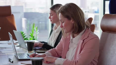 Close-up-of-a-confident-blonde-girl-with-a-bob-hairstyle-in-a-pink-business-suit-sits-at-a-table-in-the-office-during-a-business-meeting-of-a-businesswoman-in-a-modern-office