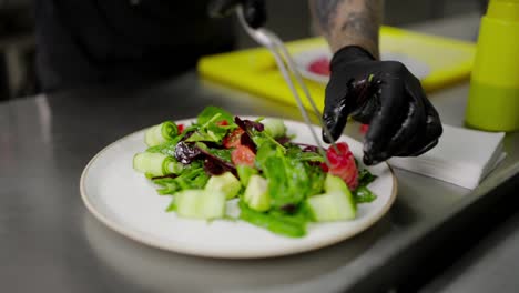 Close-up-shot-of-a-confident-male-chef-placing-the-last-pieces-of-vegetables-and-fish-on-a-salad-plate-making-the-finishing-touches-before-serving-the-dish-to-the-restaurant-hall