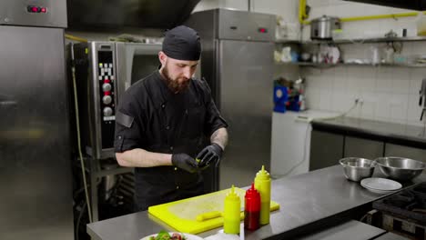 Confident-male-chef-in-a-black-uniform-with-a-beard-and-bandana-catches-a-lemon-from-his-friend-the-chef-and-puts-the-ingredient-on-a-dish-plate-in-the-kitchen