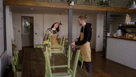 A-happy-brunette-girl-and-a-blond-guy-are-cleaning-and-preparing-for-opening-in-the-cafe-hall-in-the-morning.-A-brunette-girl-waiter-communicates-with-a-guy-during-the-start-of-the-working-day