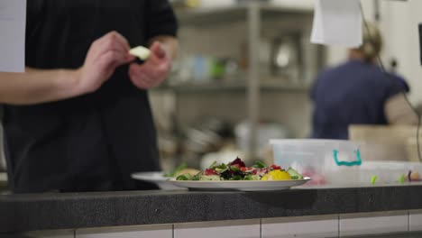 Close-up-of-a-confident-male-cook-placing-a-finished-dish-on-a-serving-table-in-a-restaurant.-A-male-chef-lays-out-a-finished-dish-ordered-for-a-restaurant-from-the-kitchen