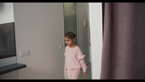 Happy-little-girl-in-pink-clothes-with-her-brother-and-parents-in-beige-clothes-walk-into-their-new-apartment-in-a-modern-style-after-moving-furnished-with-a-lot-of-boxes