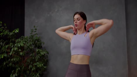 Confident-athletic-brunette-girl-in-a-purple-sports-top-does-sports-and-raises-her-knees-to-her-elbows-in-a-modern-apartment-near-a-large-indoor-plant