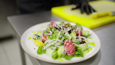 Nahaufnahme:-Ein-Männlicher-Koch-In-Schwarzen-Gummischutzhandschuhen-Bestreut-Den-Zubereiteten-Salat-Mit-Sesamkörnern-Und-Gewürzen,-Bevor-Er-Ihn-In-Der-Restaurantküche-Serviert