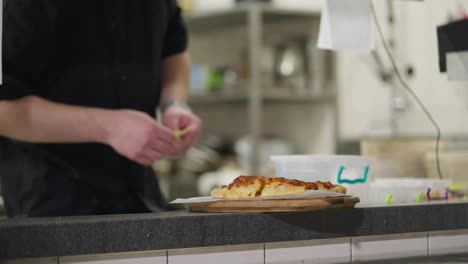 Nahaufnahme:-Ein-Koch-In-Schwarzer-Uniform-Legt-Auf-Bestellung-Ein-Fertig-Zubereitetes-Gericht-Auf-Den-Tisch,-Das-In-Einem-Restaurant-Aus-Der-Küche-Verteilt-Wird.-Ein-Professioneller-Koch-Legt-Das-Fertige-Gericht-Aus-Und-Benachrichtigt-Sie,-Dass-Es-Fertig-Ist