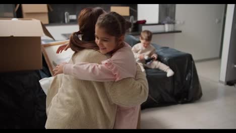 Happy-little-girl-in-pink-clothes-runs-to-her-brunette-mom-in-a-beige-sweater-and-hugs-her-then-hugs-her-dad-in-a-modern-apartment-after-moving.-Happy-children-rejoice-in-moving-to-a-new-apartment-with-their-parents-and-hugging