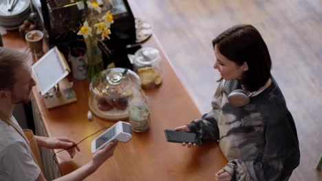 Top-view-close-up-of-a-brunette-girl-in-a-gray-sweater-paying-for-an-order-at-the-counter-using-a-terminal-in-a-cafe