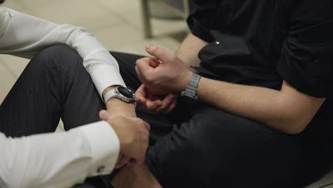 Close-up-of-a-guy-waiter-in-a-white-shirt-supports-a-professional-cook-and-pats-him-as-a-sign-of-support-while-sitting-on-the-floor-in-the-kitchen-in-a-restaurant