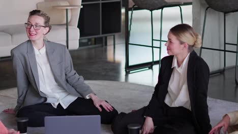 A-group-of-confident-blonde-Business-Women-in-business-suits-sit-on-the-carpet-in-the-office-and-communicate-during-their-break-at-work